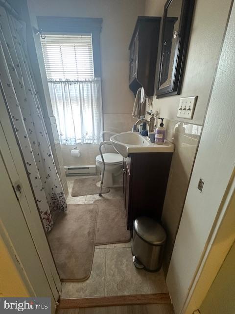 full bathroom featuring toilet, tile patterned floors, curtained shower, vanity, and a baseboard heating unit