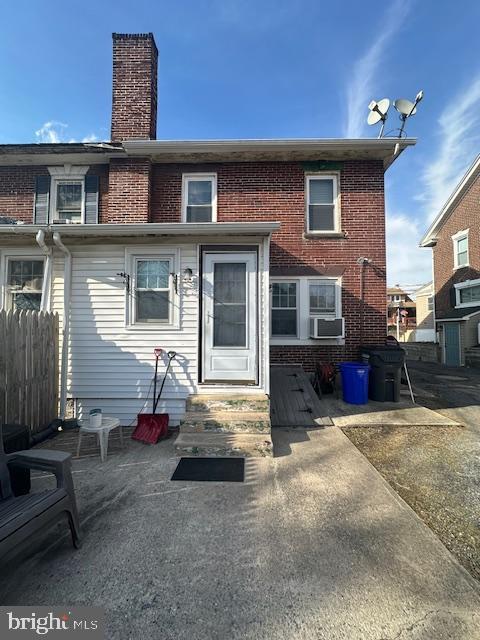 rear view of house featuring entry steps, cooling unit, brick siding, fence, and a chimney