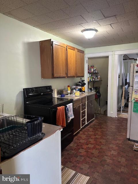 kitchen featuring black range with electric cooktop, brown cabinetry, light countertops, and freestanding refrigerator