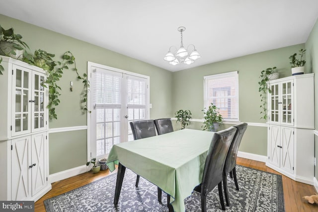 dining space featuring baseboards, a notable chandelier, a healthy amount of sunlight, and wood finished floors