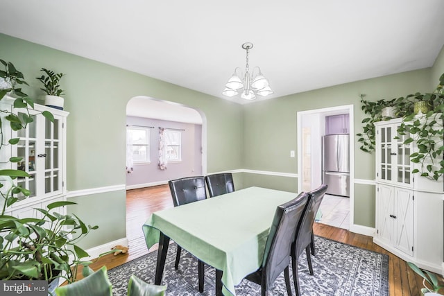 dining space with arched walkways, a chandelier, baseboards, and wood finished floors