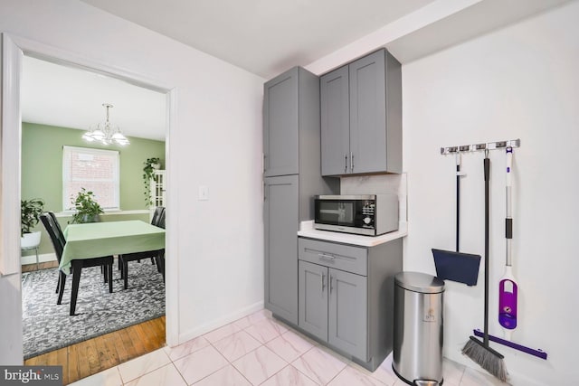 kitchen featuring an inviting chandelier, stainless steel microwave, baseboards, and gray cabinets