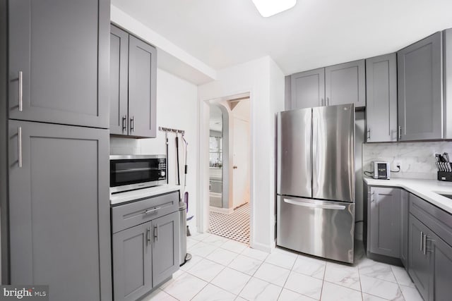 kitchen with tasteful backsplash, gray cabinetry, light countertops, appliances with stainless steel finishes, and arched walkways