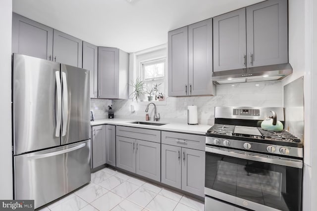 kitchen with gray cabinetry, under cabinet range hood, marble finish floor, stainless steel appliances, and a sink