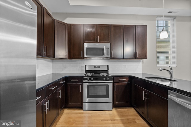 kitchen with a sink, appliances with stainless steel finishes, backsplash, light wood finished floors, and dark stone countertops