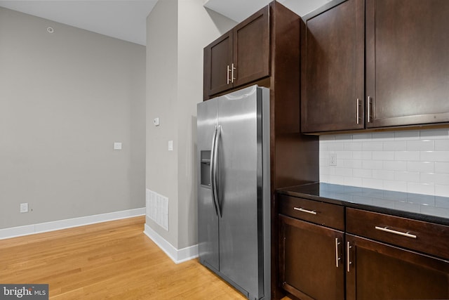 kitchen with stainless steel fridge, visible vents, decorative backsplash, dark brown cabinets, and light wood-type flooring