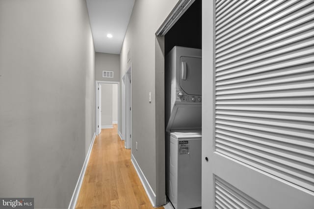 hallway featuring baseboards, light wood-style flooring, visible vents, and stacked washer / drying machine