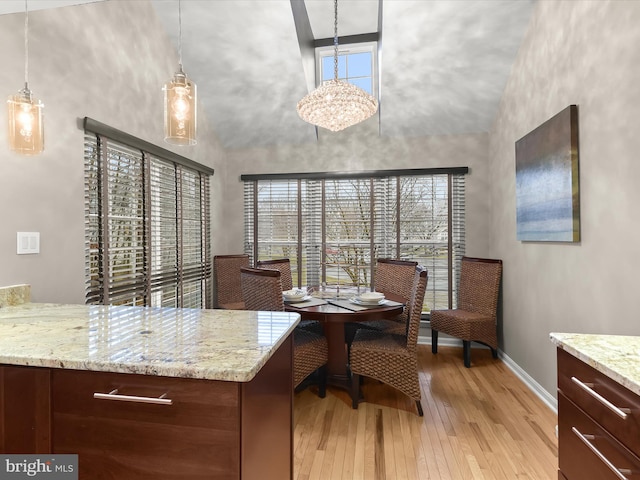 dining area with light wood-type flooring, a towering ceiling, and baseboards