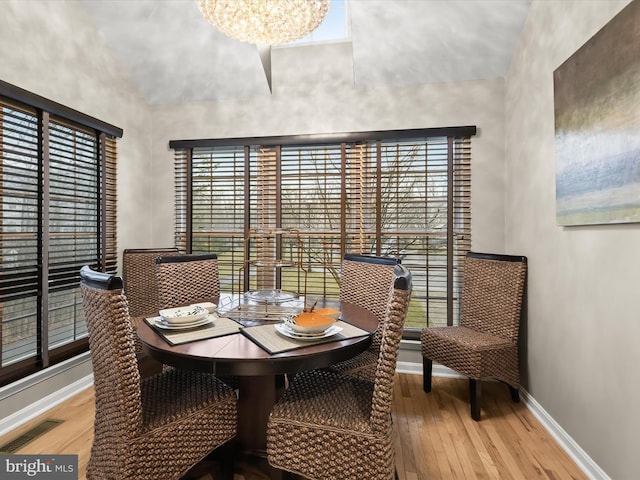 dining room with hardwood / wood-style flooring, a notable chandelier, a high ceiling, visible vents, and baseboards