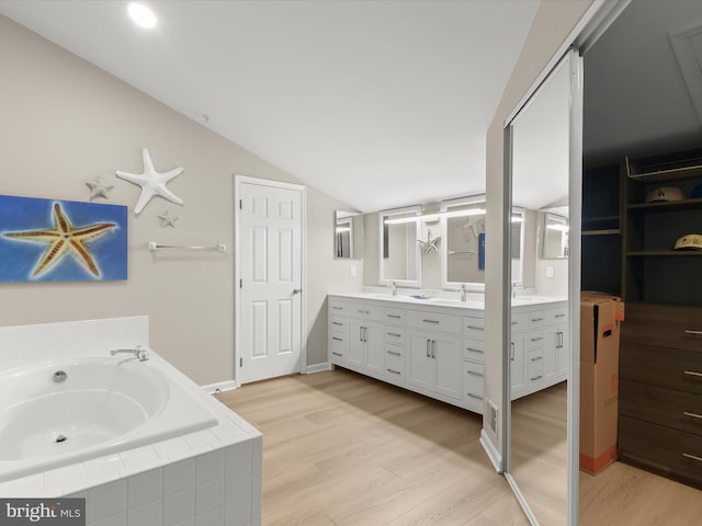 bathroom featuring double vanity, a sink, vaulted ceiling, wood finished floors, and a bath