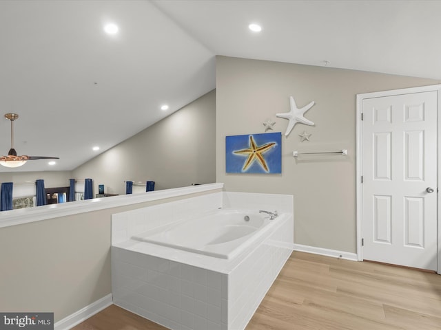 bathroom with lofted ceiling, recessed lighting, wood finished floors, baseboards, and a bath