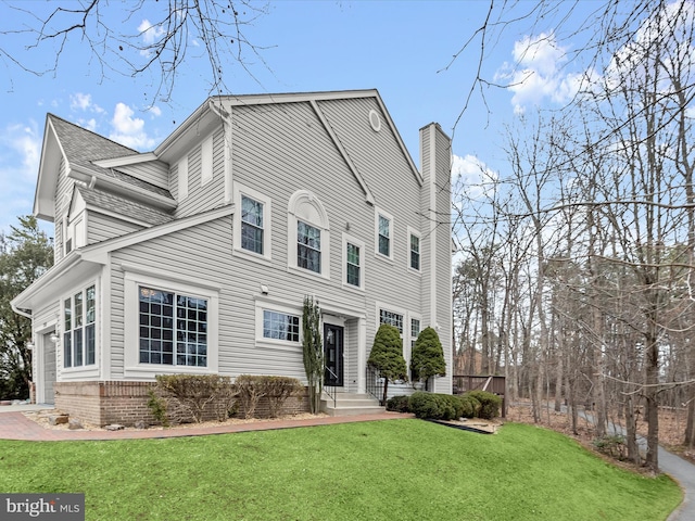 view of front of house with brick siding, a chimney, a shingled roof, a front yard, and a garage