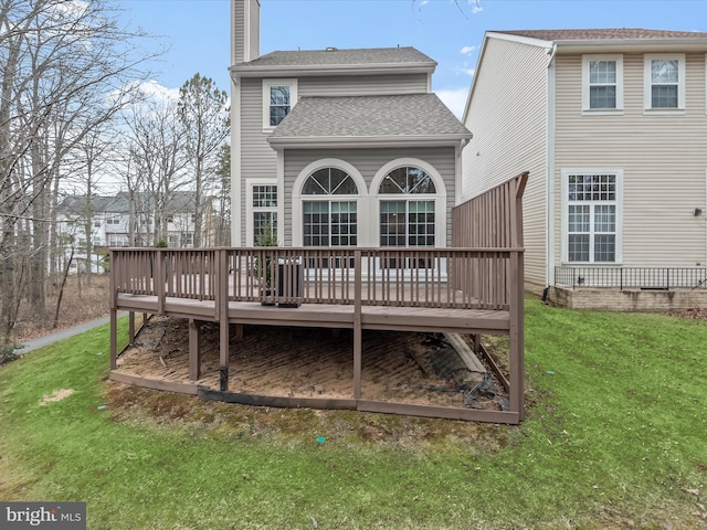 rear view of property with a shingled roof, a chimney, a deck, and a yard