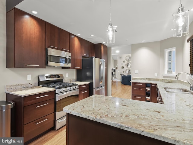 kitchen featuring stainless steel appliances, a sink, hanging light fixtures, and light stone countertops