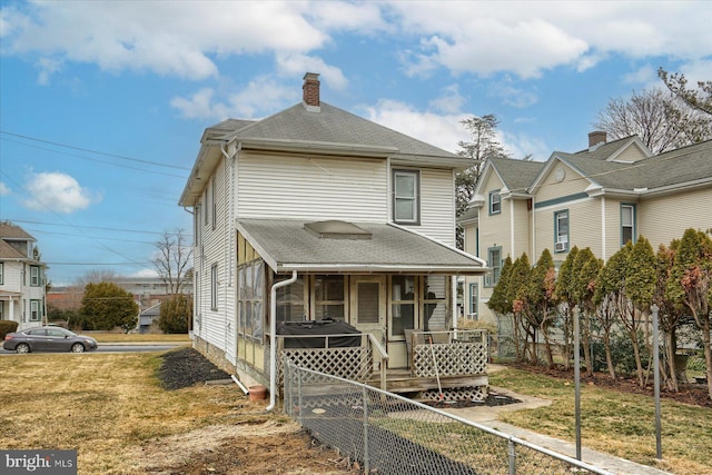 view of front facade featuring roof with shingles, a front lawn, a chimney, and fence