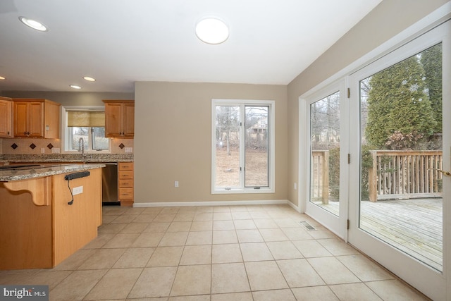 kitchen featuring light stone counters, light tile patterned flooring, a breakfast bar, stainless steel dishwasher, and tasteful backsplash