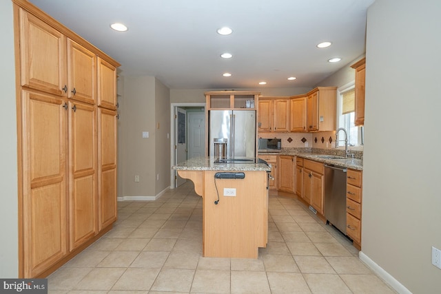 kitchen with light tile patterned floors, light stone counters, stainless steel appliances, a sink, and a center island