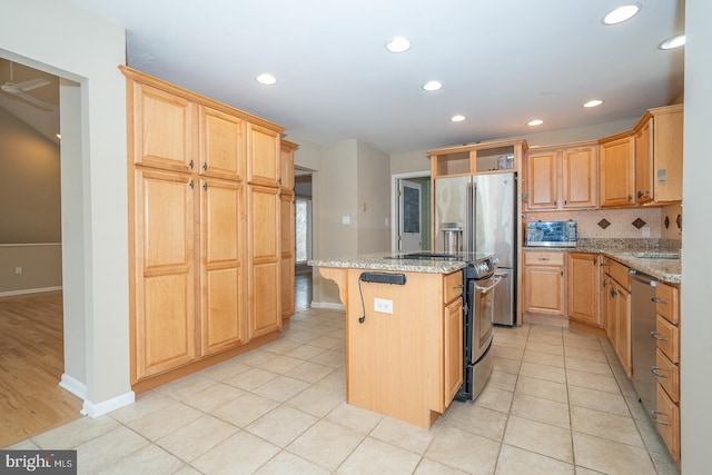 kitchen with light tile patterned floors, a kitchen island, appliances with stainless steel finishes, light stone counters, and backsplash