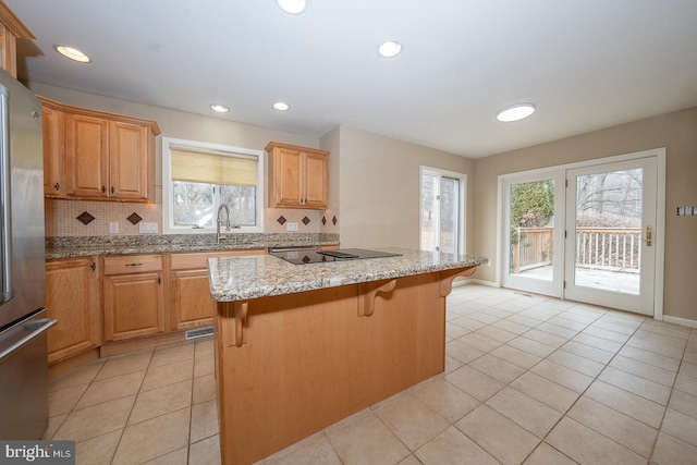 kitchen with black electric cooktop, a kitchen island, decorative backsplash, freestanding refrigerator, and light stone countertops