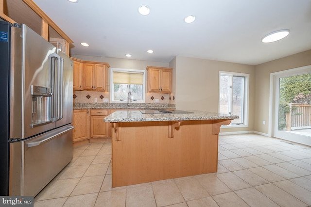 kitchen with black electric stovetop, light tile patterned floors, high end fridge, a kitchen island, and a kitchen breakfast bar