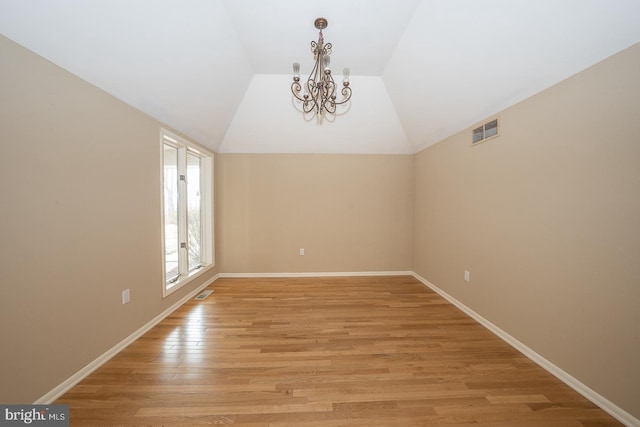 unfurnished room featuring light wood finished floors, baseboards, visible vents, vaulted ceiling, and a chandelier