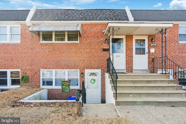 property entrance featuring roof with shingles and brick siding