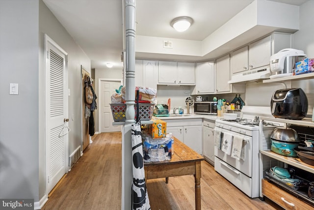 kitchen featuring light wood-style flooring, stainless steel microwave, light countertops, under cabinet range hood, and gas range gas stove