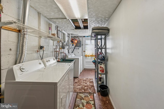 clothes washing area with laundry area, washing machine and clothes dryer, and concrete block wall