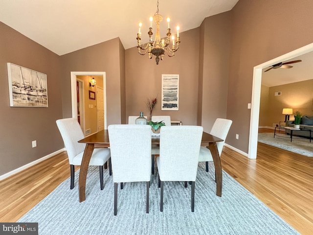 dining space featuring light wood finished floors, ceiling fan with notable chandelier, baseboards, and lofted ceiling