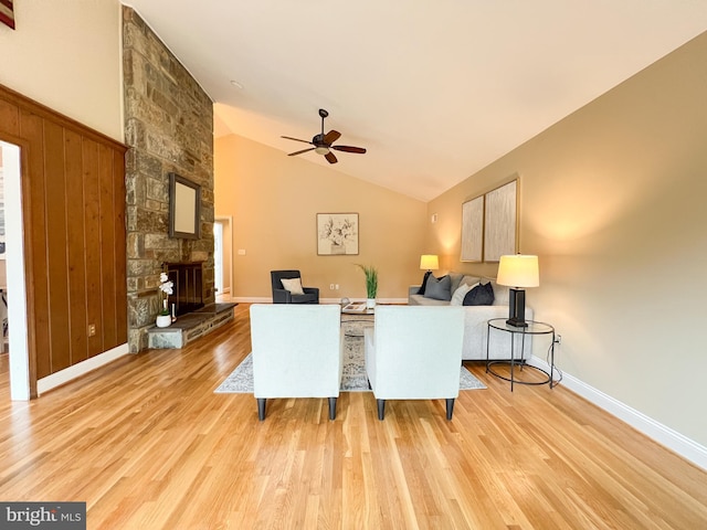 living area with ceiling fan, baseboards, lofted ceiling, a stone fireplace, and wood finished floors