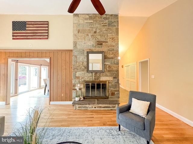 living area with a stone fireplace, high vaulted ceiling, baseboards, and wood finished floors