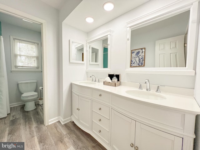 full bath with double vanity, toilet, wood finished floors, and a sink