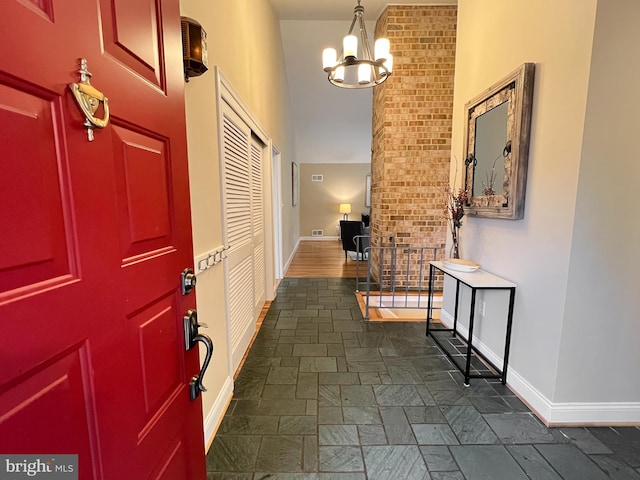 entryway featuring baseboards, an inviting chandelier, a towering ceiling, and stone finish floor