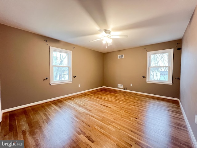 unfurnished room with visible vents, baseboards, wood finished floors, and a ceiling fan