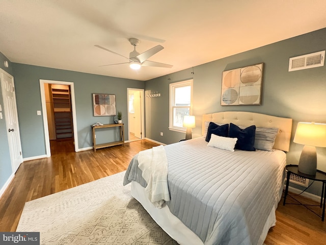 bedroom with visible vents, baseboards, a walk in closet, and wood finished floors