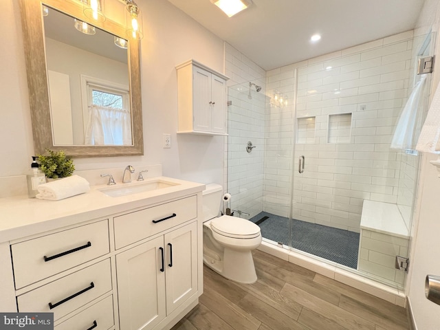 bathroom featuring wood finished floors, toilet, a stall shower, and vanity