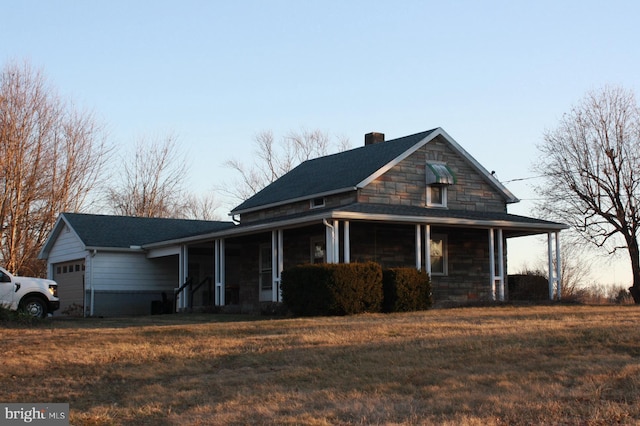 farmhouse inspired home with covered porch, a garage, stone siding, a chimney, and a front yard