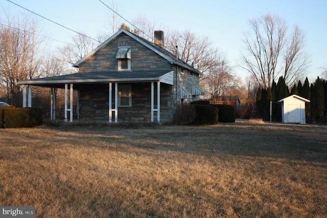 view of front facade featuring stone siding, a porch, a chimney, and a front lawn