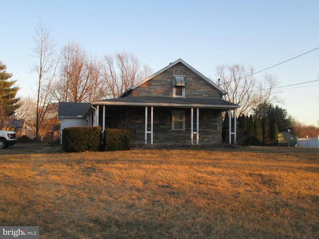 view of front of property with a garage, stone siding, a porch, and a front yard