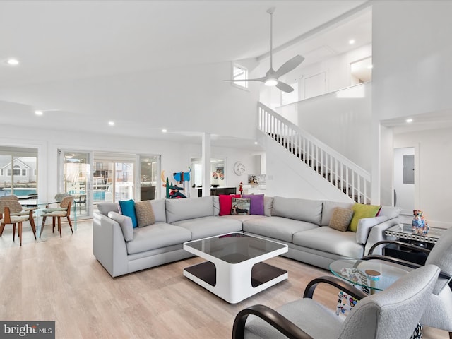 living area with light wood finished floors, a ceiling fan, stairs, a high ceiling, and recessed lighting