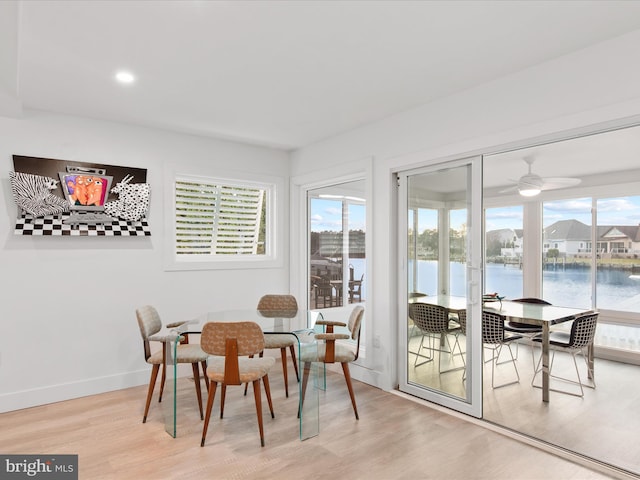 dining area with light wood-style flooring, a water view, a wealth of natural light, and baseboards