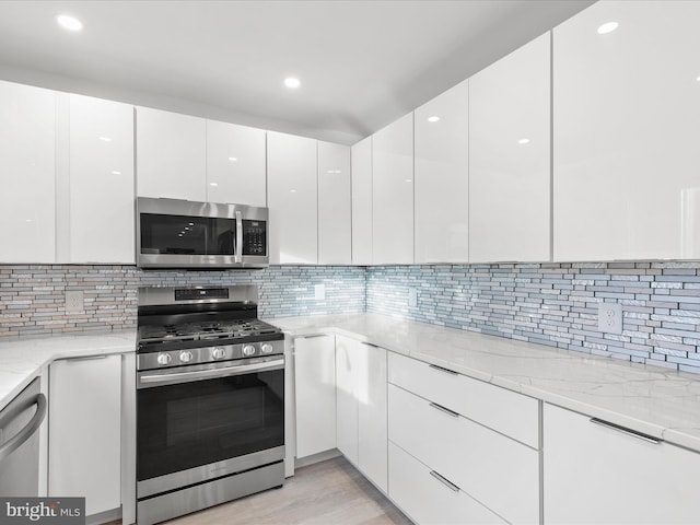 kitchen with light wood-style flooring, modern cabinets, appliances with stainless steel finishes, light stone counters, and white cabinetry