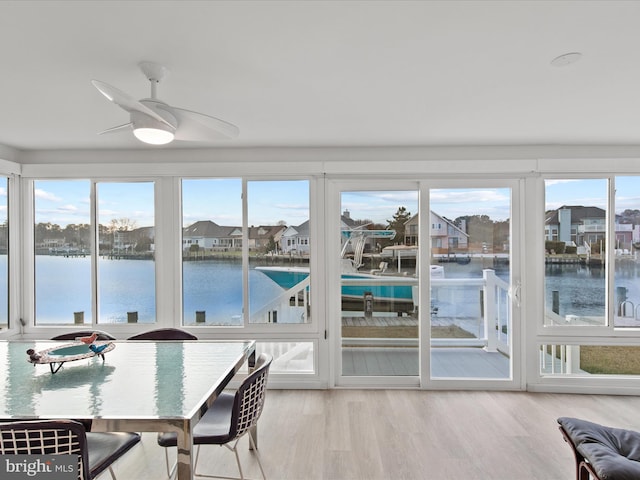 sunroom featuring ceiling fan, plenty of natural light, a residential view, and a water view