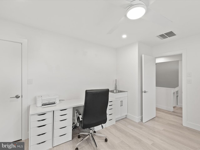 home office with light wood finished floors, baseboards, visible vents, and a sink