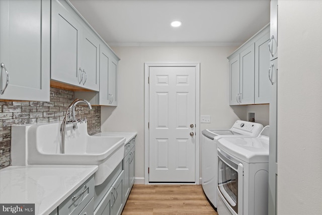 laundry room with cabinet space, ornamental molding, independent washer and dryer, light wood-type flooring, and a sink