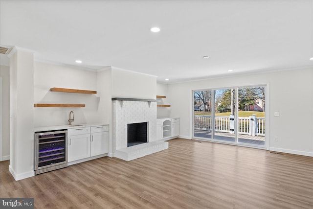 unfurnished living room with baseboards, light wood-style flooring, wine cooler, ornamental molding, and a brick fireplace