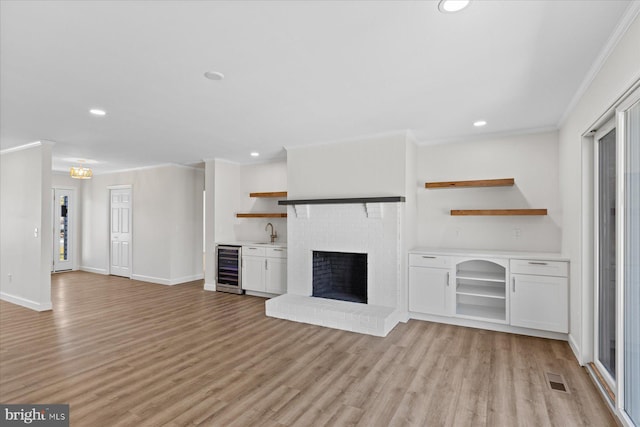 unfurnished living room with beverage cooler, baseboards, light wood-style flooring, and crown molding