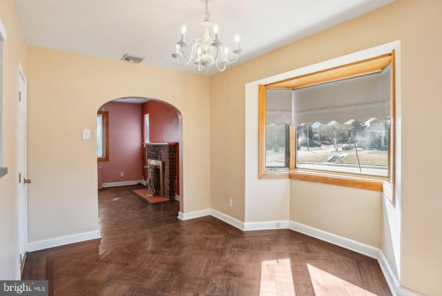 unfurnished dining area featuring baseboards, visible vents, arched walkways, an inviting chandelier, and a fireplace