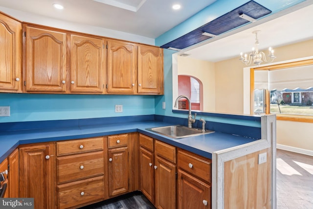 kitchen featuring a chandelier, a peninsula, a sink, hanging light fixtures, and brown cabinets