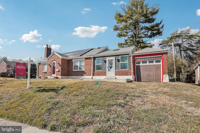 single story home featuring brick siding, a chimney, a front yard, roof mounted solar panels, and a garage